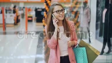 好看的小姐正在手机上说话，独自走在商场里拎着纸袋.. 新衣服